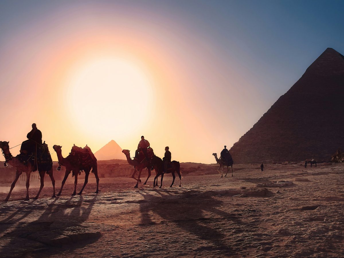 Camel riders crossing the Giza plateau at sunset
