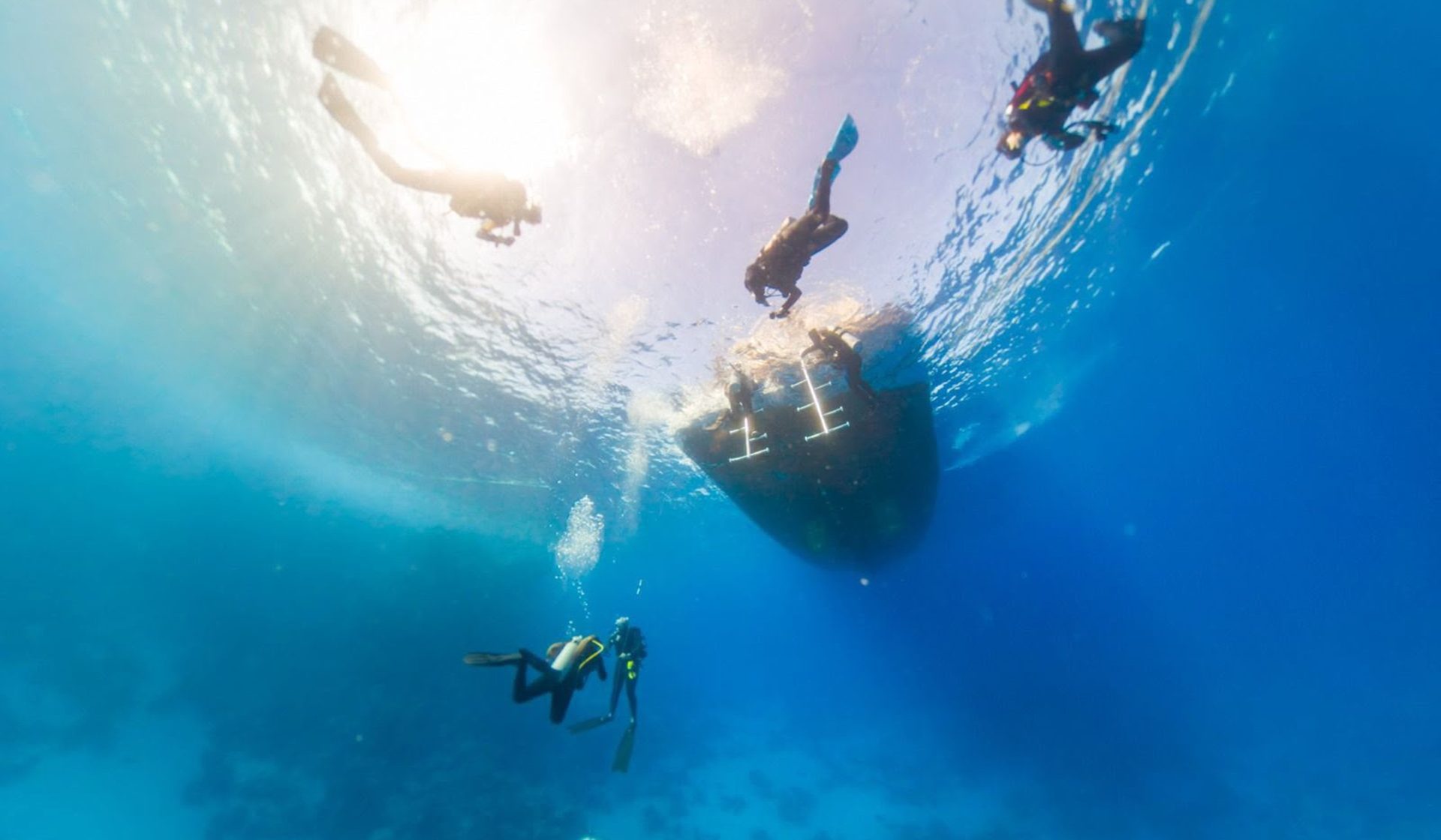 Scuba divers descending beneath a boat in clear Red Sea water
